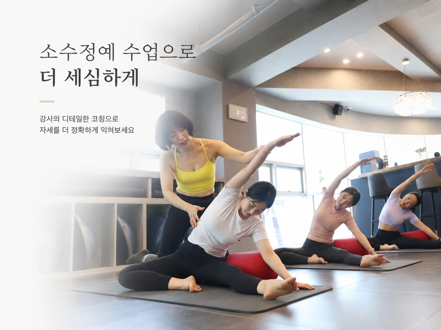 달망필라테스 강사가 소수정원 회원의 자세를 확인하며 옆구리 스트레칭 동작을 지도하는 모습
