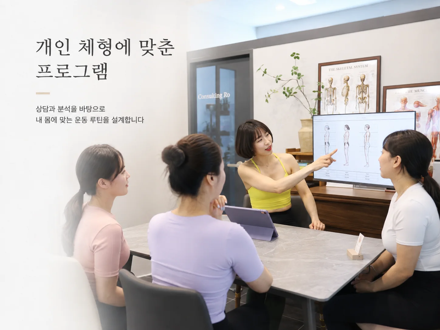 강사가 해부학 자료를 보며 회원들과 개인별 운동 방향을 상담하는 모습